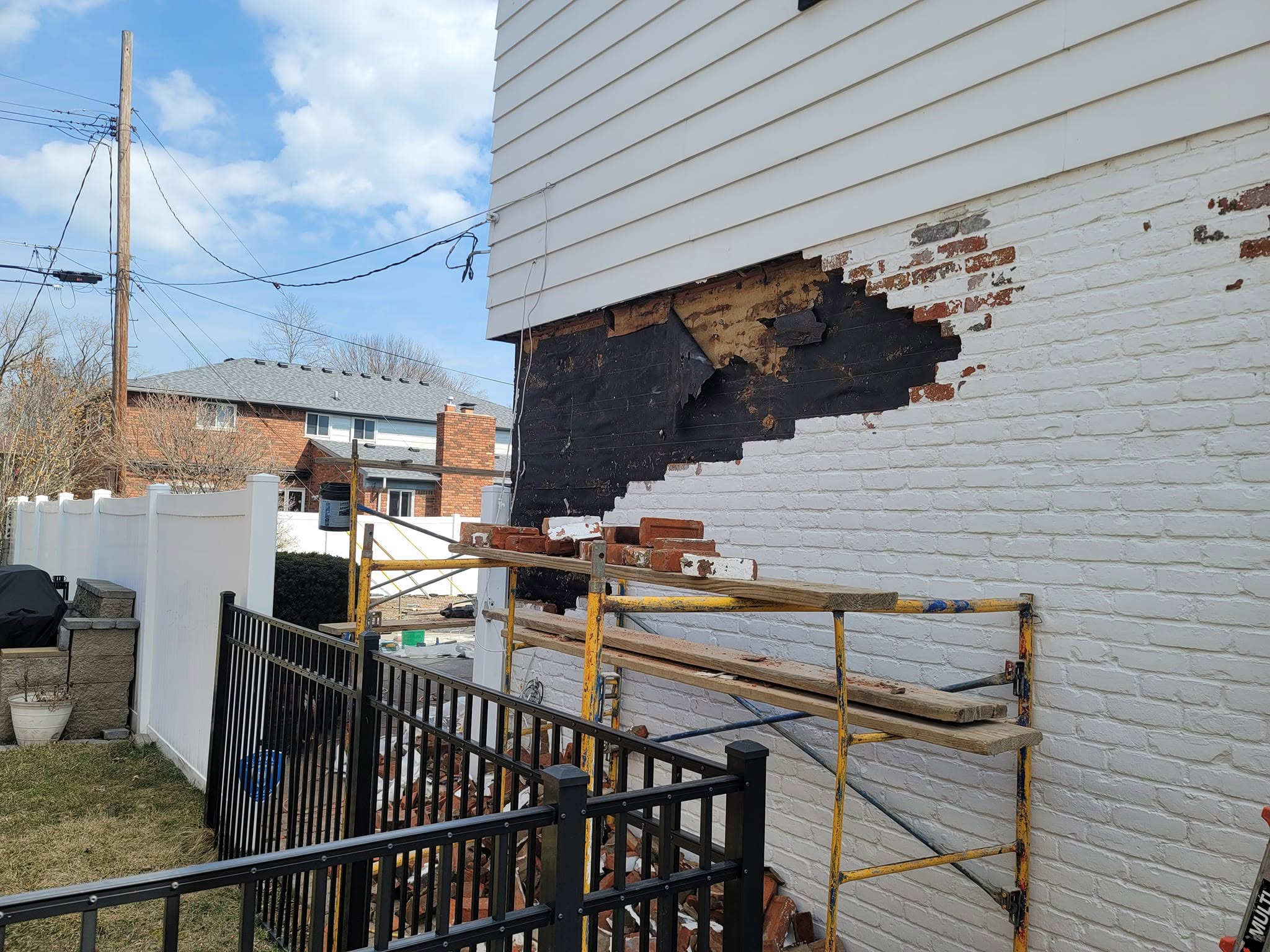 House wall during brick repair in Grosse Pointe Woods, with bricks removed beneath the siding