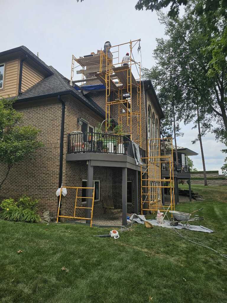 Skyline crew member working at a chimney from yellow scaffolding beside a brick house