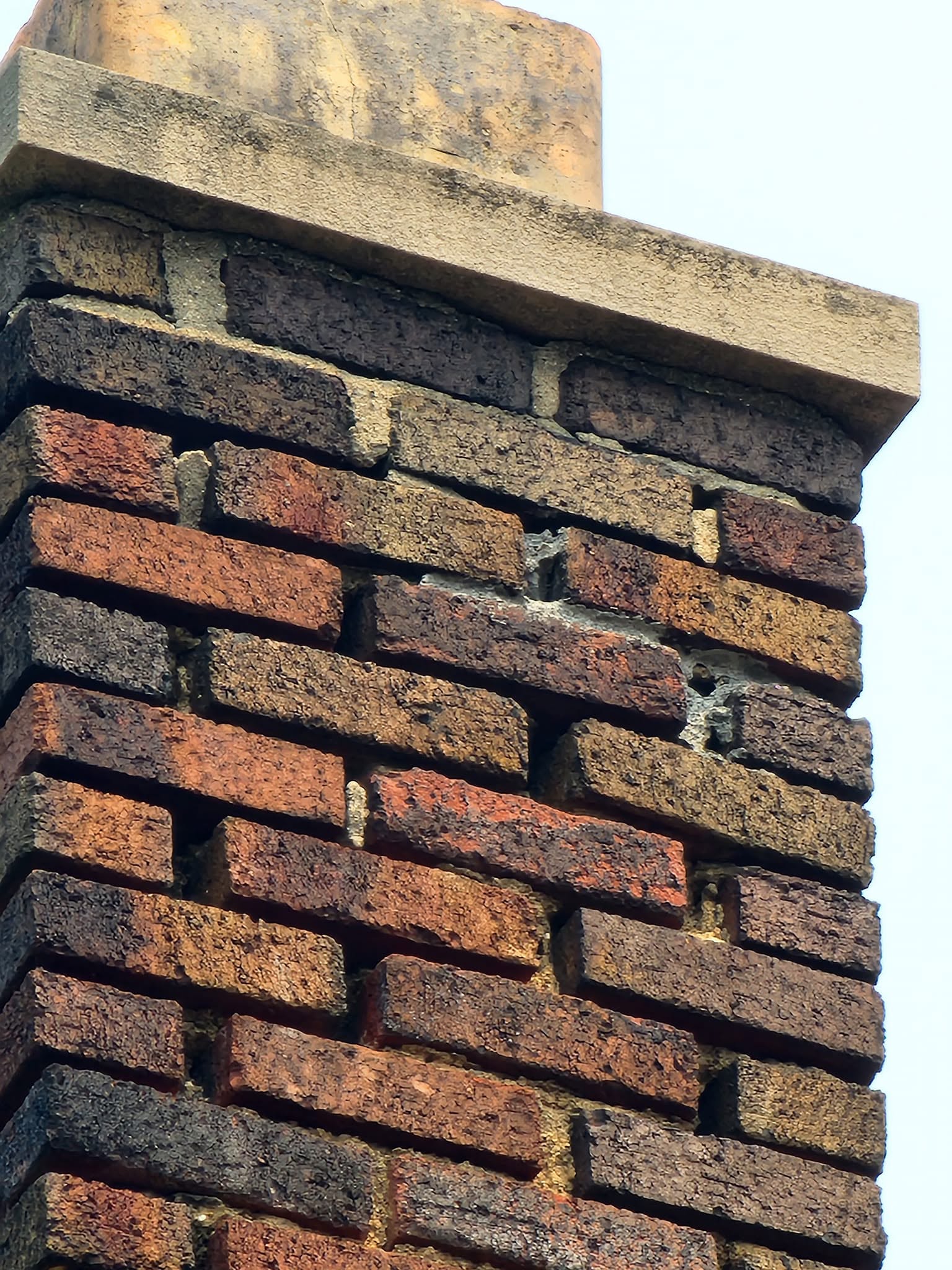 Weathered chimney bricks with deep gaps and worn mortar beneath the crown